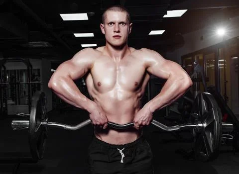 Athletic young man doing exercises with barbell in gym. Handsome muscular bod Foto stock