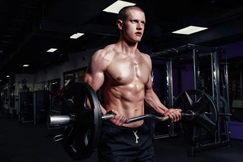 Athletic young man doing exercises with barbell in gym. Handsome muscular bod Stock Photos