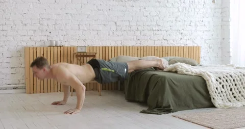 Athletic young man doing push ups exercise with legs on bed at home, side view. Stock Footage 146681088