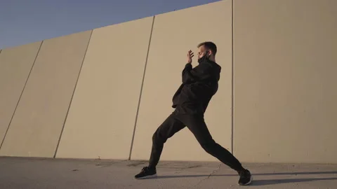 Athletic young man dressed in black dancing contemporary in front of a gray w Stock Footage 143614528