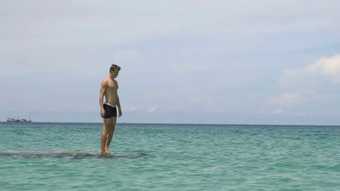 Athletic young man jumping from stone into ocean sea blue water. Stock Footage 76010510