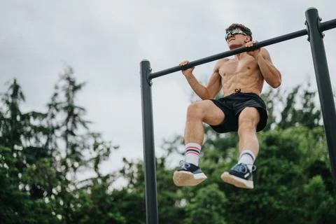 Athletic young man performing a pull-up on outdoor parallel bars Foto stock