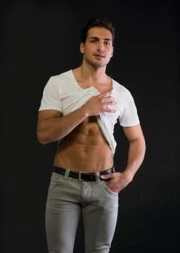Athletic young man pulling up white t-shirt to show abs Stock Photos