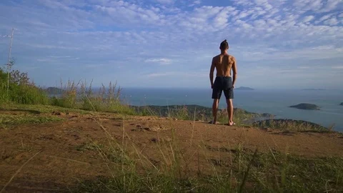 Athletic young man raises his hands up standing on the edge of the mountain. Video stock 83292939