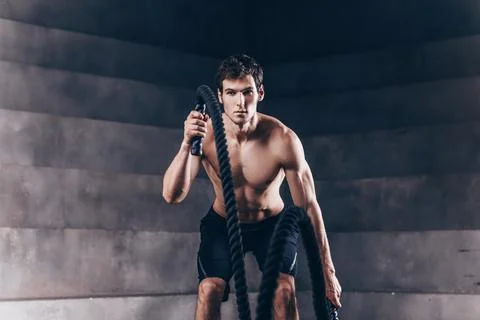 Athletic young man with rope doing exercise in functional training fitness gy Stock Photos