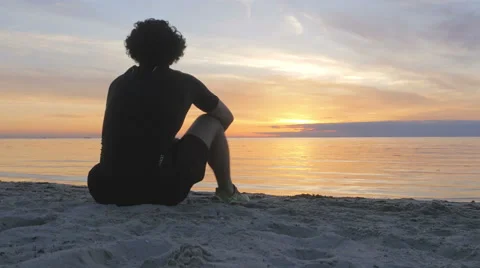 Athletic young man sitting on the beach at sunset Stock Footage 51466309