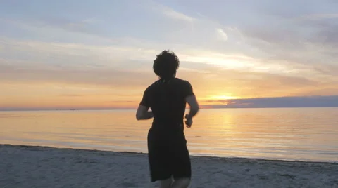 Athletic young man sitting on the beach at sunset Stock Footage 51467131