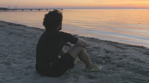 Athletic young man sitting on the beach at sunset Stockbeeldmateriaal 51467391