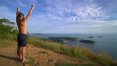 Athletic young man stands with his hands up on the edge of the mountain. Stock Footage 83292957