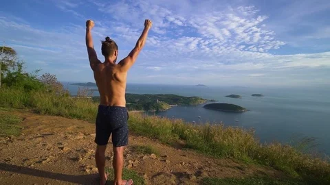 Athletic young man stands with his hands up on the edge of the mountain. Video stock 83292968