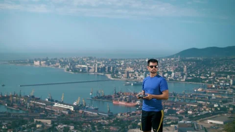 Athletic young man stands with a quadrocopter control panel on top of a hill Stock Footage 128743961