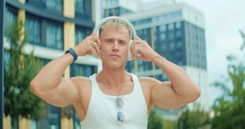 Athletic young man turns on wireless headphones, smiles, and enjoys music Stock Footage 303597557