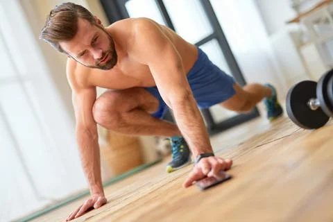 Athletic young man using smartphone during home workout Stock Photos