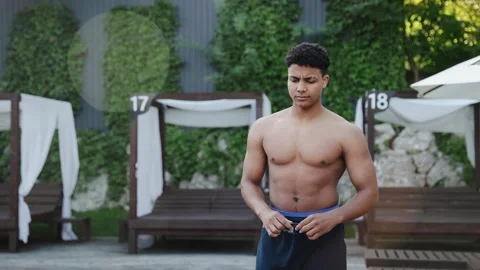 Athletic young man walking shirtless near pool, contemplating fitness lifestyle Stock Footage 333564884