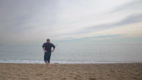 Athletic Young Man Walks Toward Water on Beach in Slow Motion Full HD Stock Footage 154973317