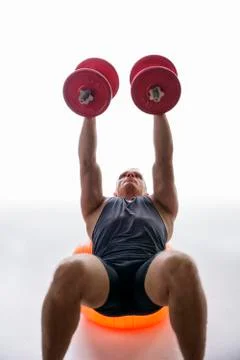 Athletic young man working out with dumbbells on gym ball Stock Photos
