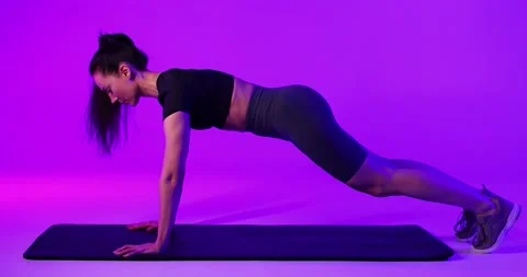 Athletic young woman doing push-ups in a studio with subdued purple lighting Vídeo Stock 233404366