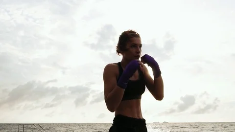 Athletic young woman shadow boxing by the sea against the sun. Beautiful female Stock Footage