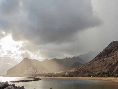 Atlantic Ocean, beach and mountains behind. From the clouds make their way rays Stock Footage 71777618