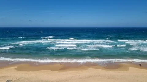 Atlantic Ocean waves breaking on sandy beach under blue sky Stock Photos