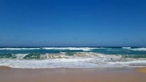 Atlantic Ocean waves breaking on sandy beach under blue sky Stock Photos