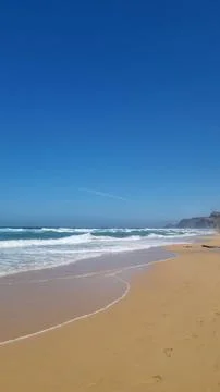 Atlantic Ocean waves breaking on sandy beach under blue sky Stock Photos