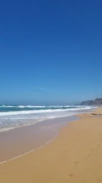 Atlantic Ocean waves breaking on sandy beach under blue sky Stock Photos