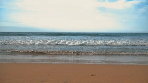 Atlantic ocean waves with foam, orange sand, and dramatic clouds blue sky Stock Footage 93464633