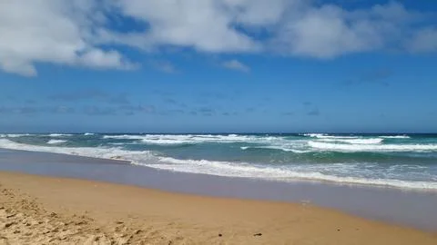 Atlantic ocean waves on a sandy beach under blue cloudy sky, Algarve, Portuga Stock Photos