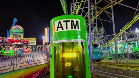 ATM machine at amusement park with roller coaster and carousel rides at night Stock Footage 344021691