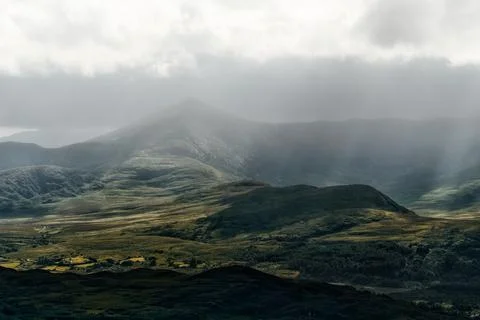 Atmospheric sunlight breaks through clouds, illuminating textured hills Stock Photos