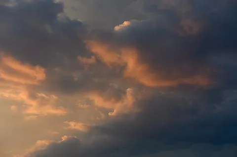 Atmospheric sunset cloudscape featuring dark clouds and warm golden light Stock Photos