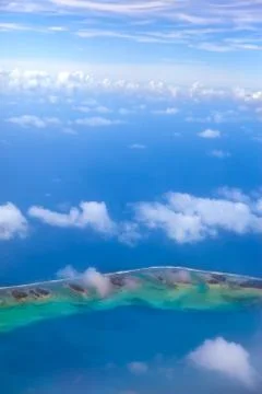 The atoll ring in ocean is visible through clouds. Aerial view... Stock Photos
