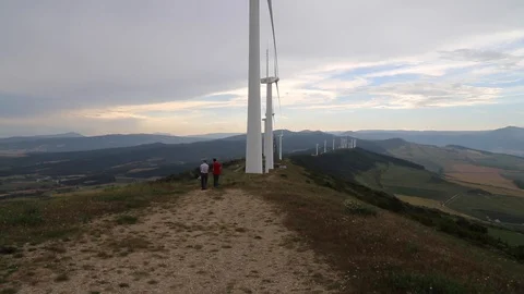 Atop a mountain, two men walk by turning windmills Stock Footage 123979665