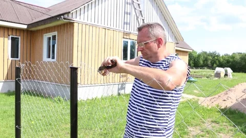 Attaching chain-link fence to posts, worker weaves ends of wire into braids.. Stock Footage 277302764