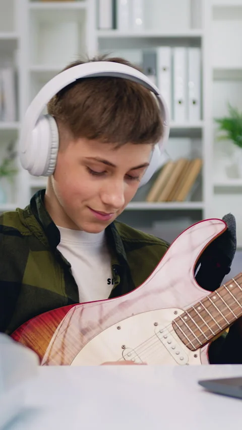 Attaractive boy in headphone is learning to play the guitar using laptop compute Stock Footage 325993222