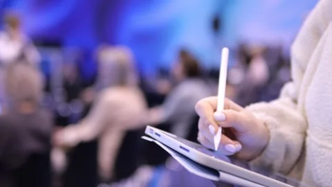 Attendee writes notes on tablet at event with soft focus on crowd Stock Footage 348588810
