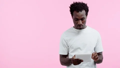 Attentive african american man using digital tablet isolated on pink Stock Footage 117994612