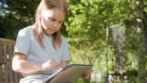 Attentive child taps digital tablet computer outside in backyard garden. Vídeo Stock 346723874