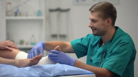 Attentive doctor checking patients elastic wrap leg, talking good rehab result Video stock 117176053