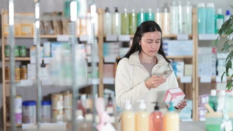 Attentive middle-aged female client controlling QR code of medicament box in Stock Footage 313877888