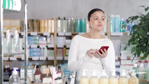 Attentive middle-aged female client scrolling phone while looking for something Stock Footage 329392250