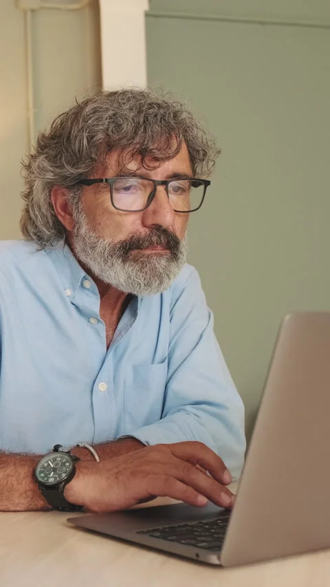 Attentive middle aged man in glasses sitting in the living room working on Stock Footage 254913239