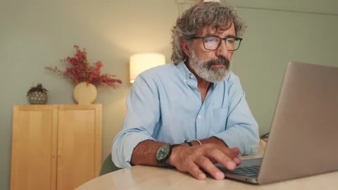 Attentive middle aged man in glasses sitting in the living room working on Stock Footage 255962968