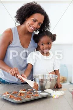 Attentive mother helping her girl cooking biscuits Stock Photos