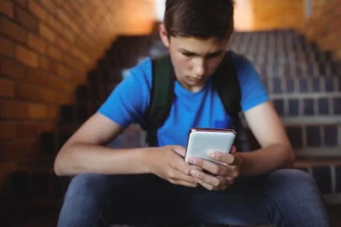 Attentive schoolboy using mobile phone on staircase 스톡 사진