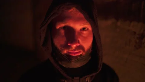 Attentive sight of a young bearded man in hood and mask near the fire Video stock 144670775