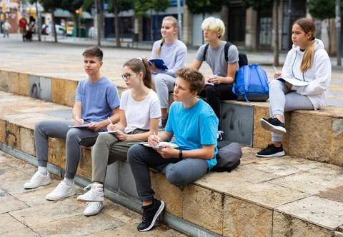 Attentive students write lesson in a notebook sitting on stone street parapet Foto stock