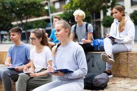 Attentive students write lesson in a notebook sitting on stone street parapet Foto stock
