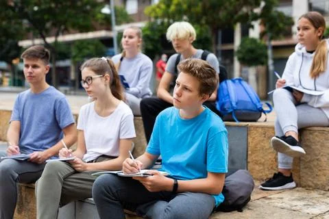 Attentive students write lesson in a notebook sitting on stone street parapet 写真素材